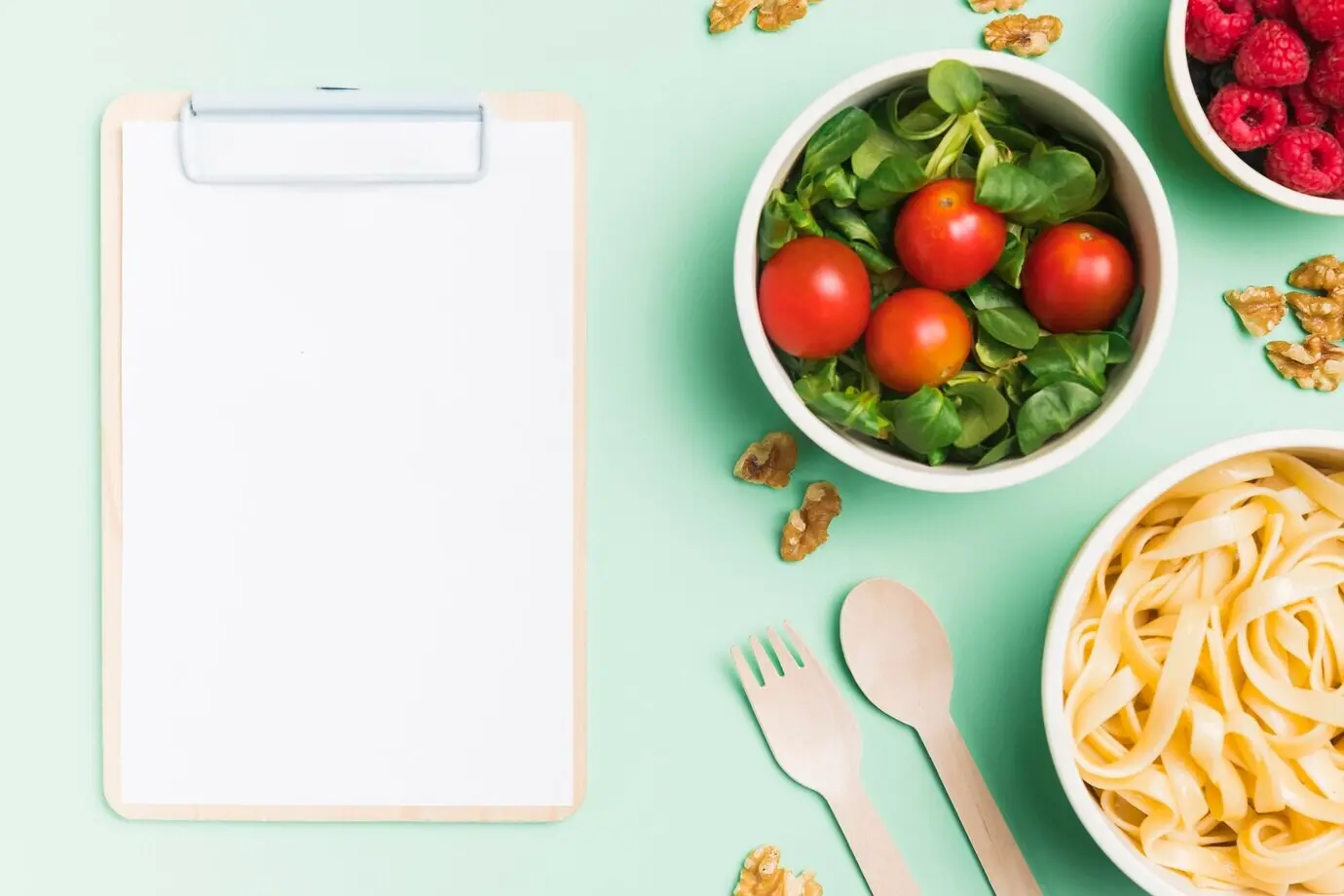 Draufsicht auf Lebensmittelbehälter mit Himbeeren, Salat und Pasta sowie ein leeres Klemmbrett.